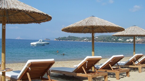 Una playa con sillones de madera y sombrillas de paja.