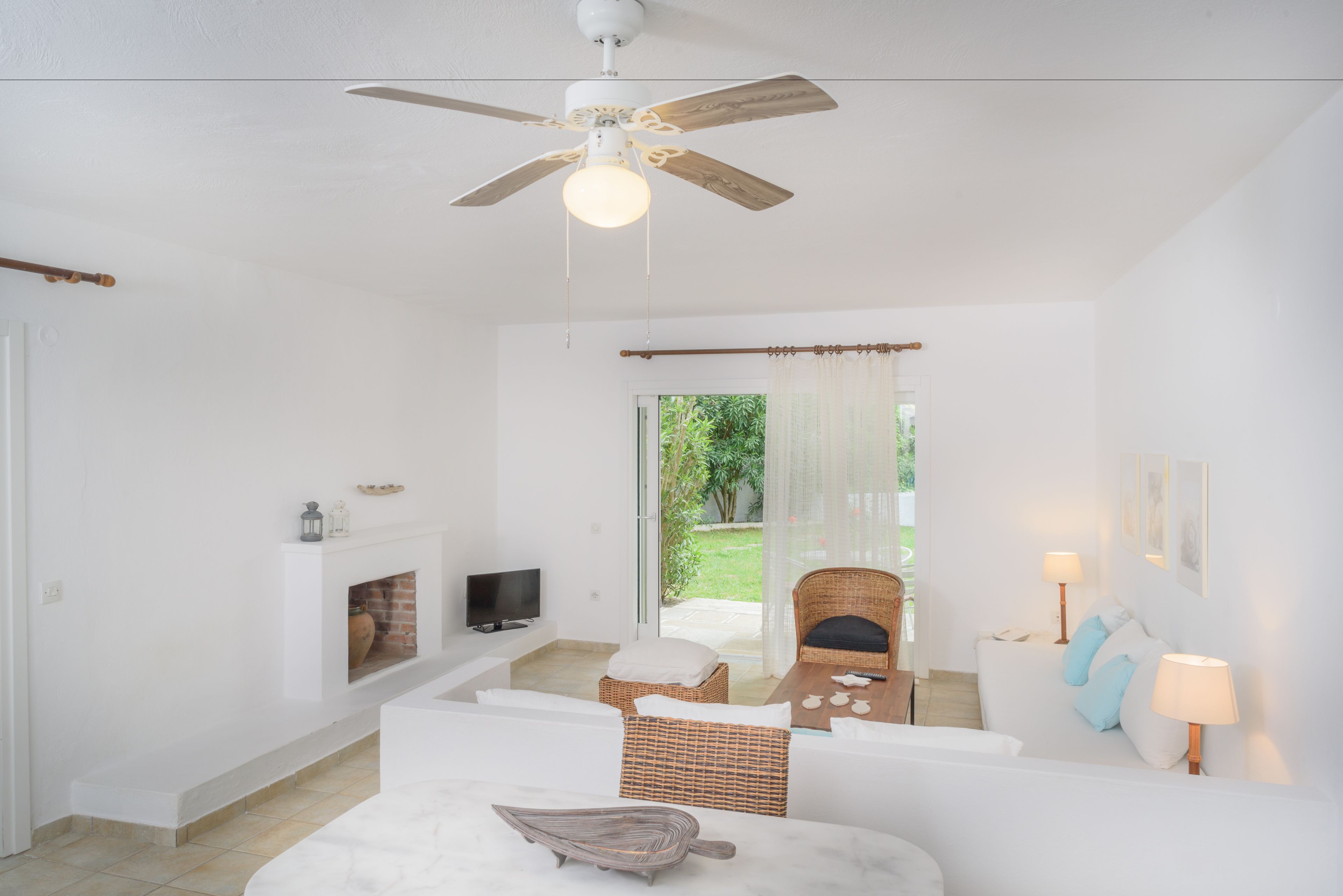 A bright, white room with a ceiling fan, a fireplace, a television, and a wicker chair.