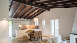 Amplia sala de estar con un sofá blanco, una mesa de comedor con sillas de mimbre, una cocina con gabinetes blancos y una chimenea.