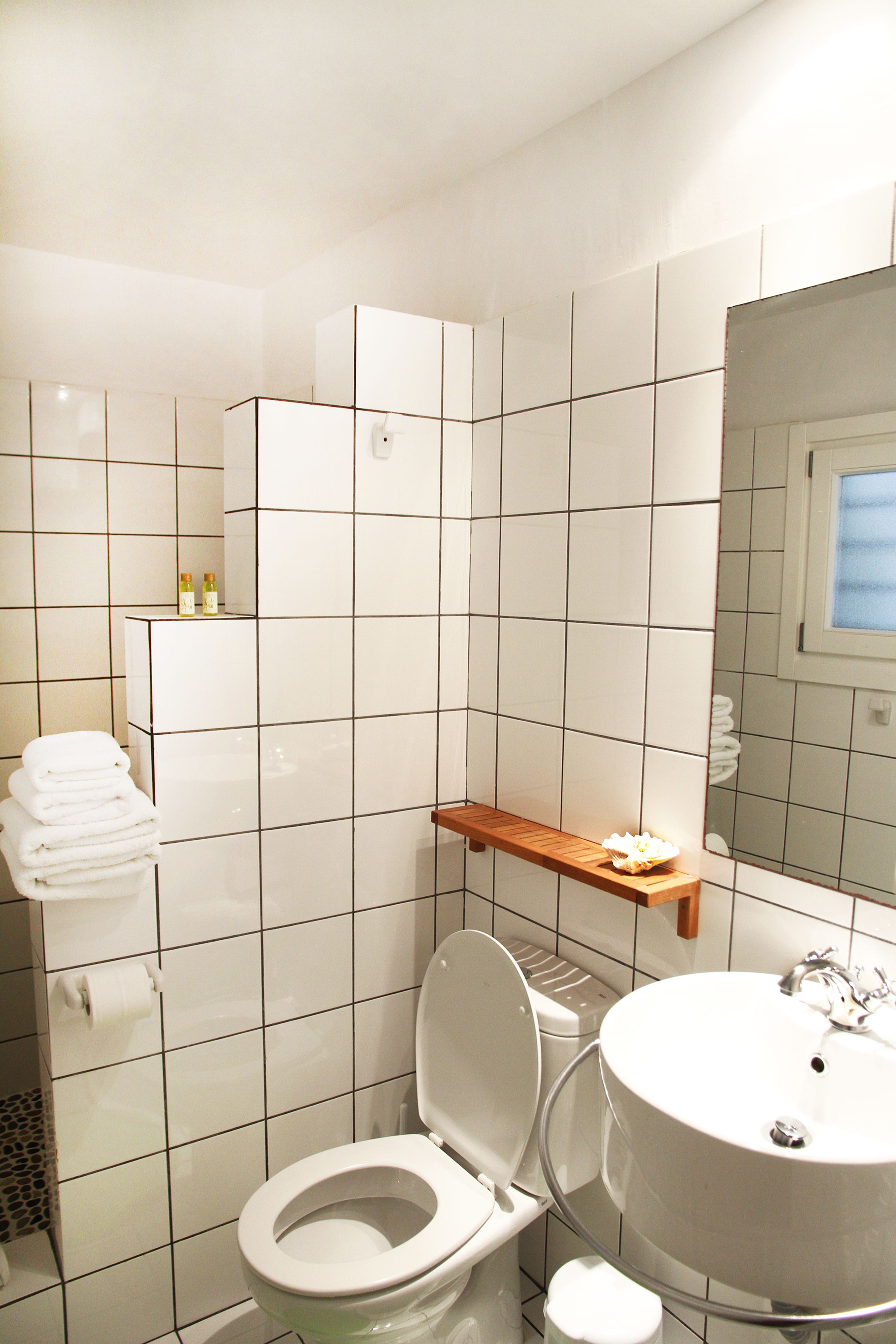 Ein Badezimmer mit weißen Fliesen, einer Toilette, einem Waschbecken und einem Spiegel.
