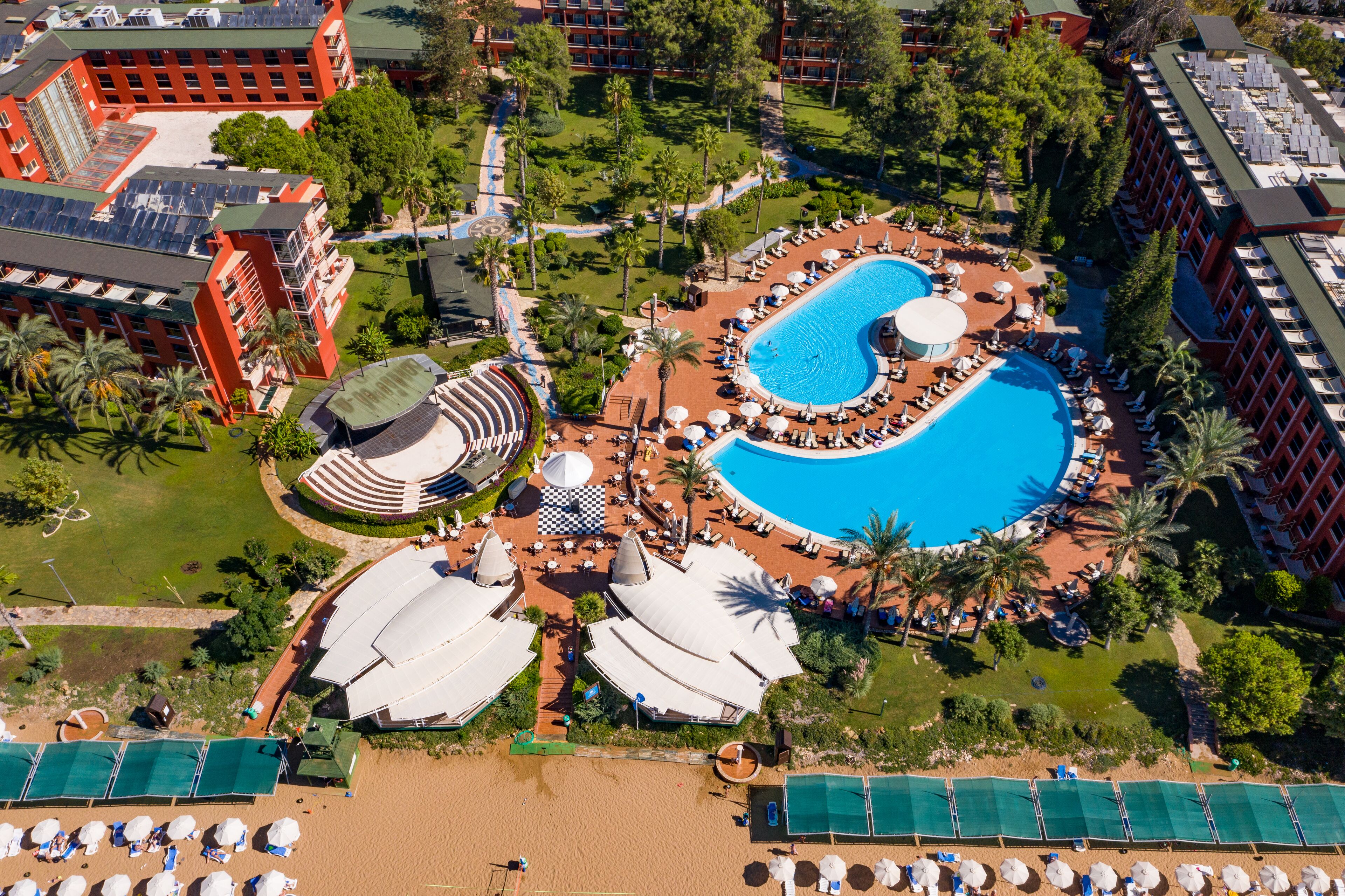 An aerial view of a resort with a large swimming pool, multiple lounge areas, and a beach with sun loungers.