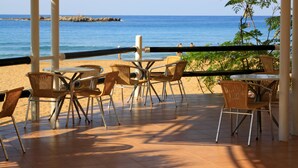 Un área de estar al aire libre con sillas y mesas de mimbre, con vista a una playa y el mar.
