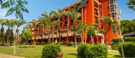 Hotel de vários andares com fachada vermelha, palmeiras e um caminho de pedra.