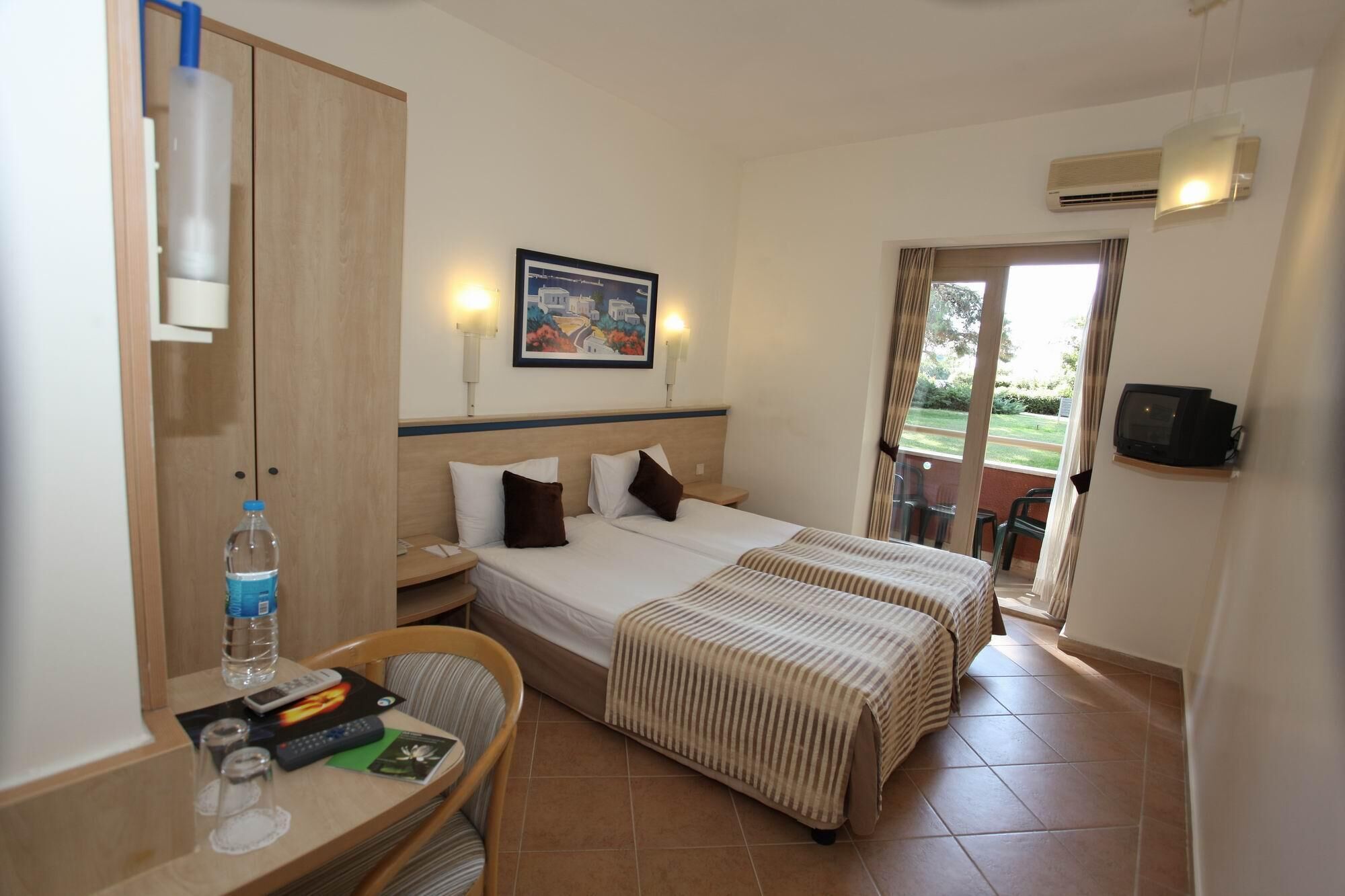 A hotel room with two beds, a desk with a chair, a TV, and a painting on the wall.