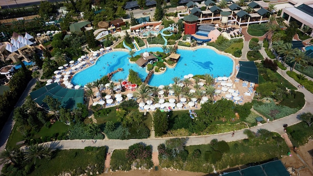 Vista aérea de un resort con varias piscinas, tumbonas y palmeras.