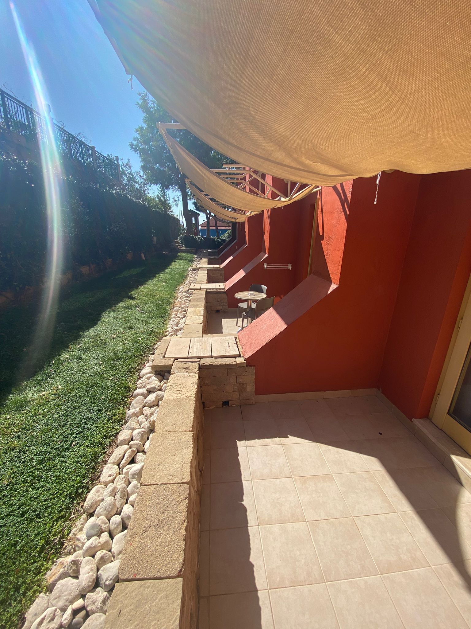 A patio with a red wall, a stone wall, and a tiled floor.