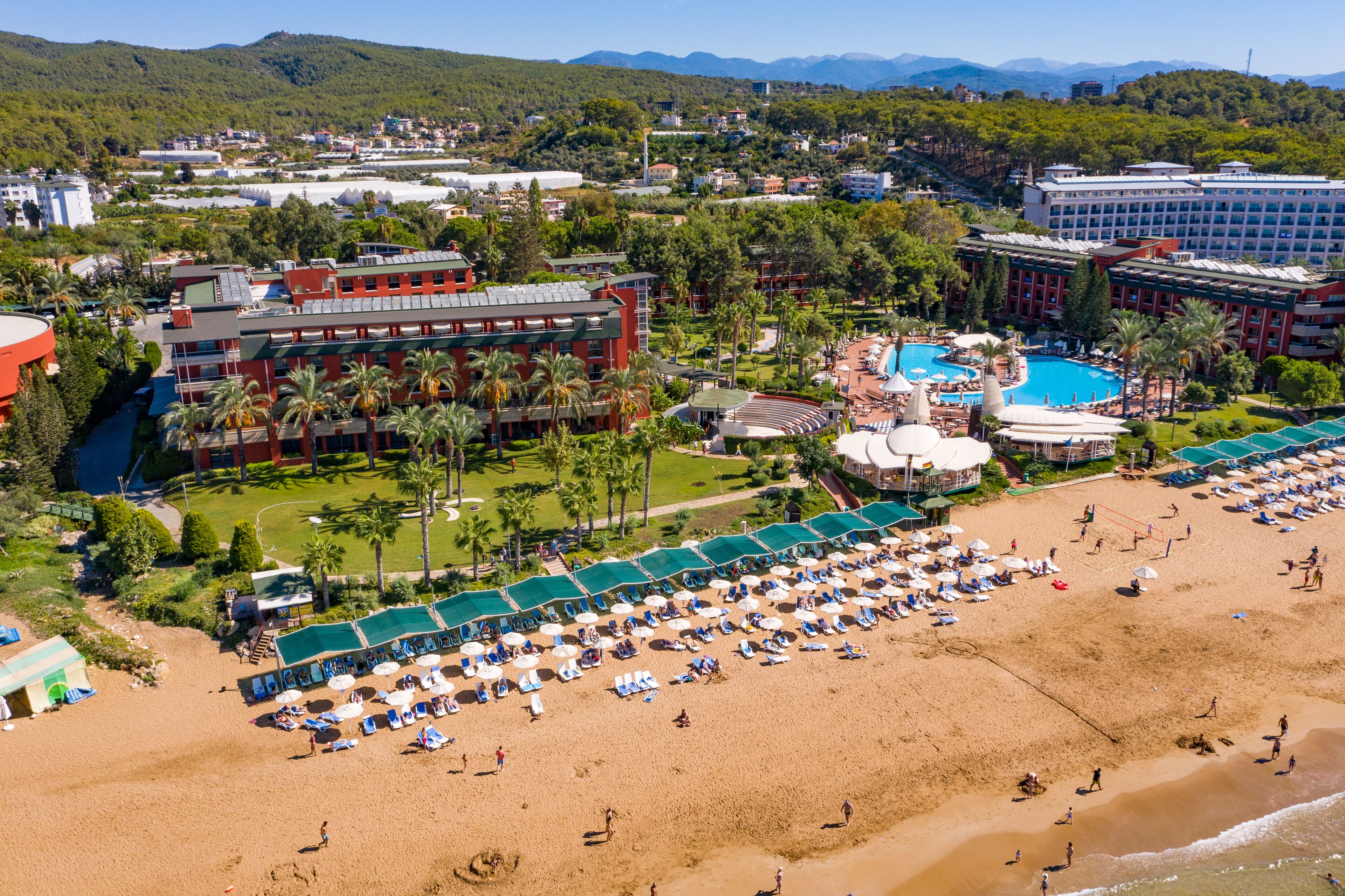 Un resort con varias construcciones, una piscina grande y una zona de playa con tumbonas y sombrillas.