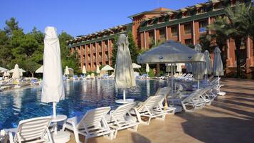 Ett hotellområde med en pool, solstolar och parasoller, omgivet av en byggnad med balkonger.