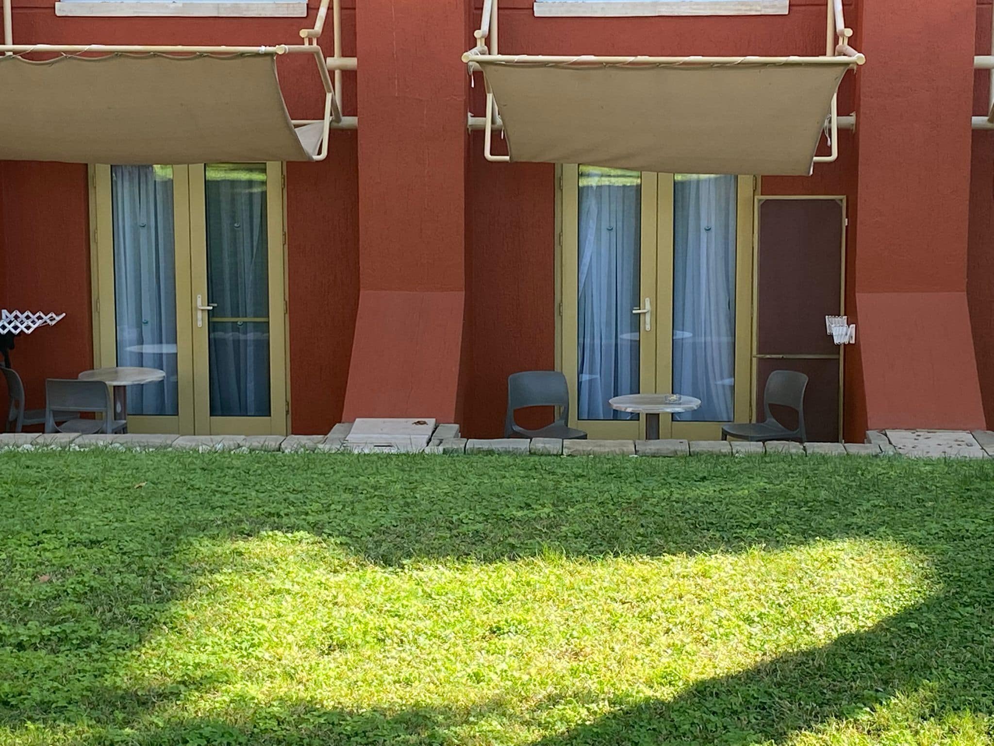 A building with two balconies, each with a table and chairs, and a grassy area in front.
