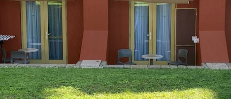 A building with two balconies, each with a table and chairs, and a grassy area in front.