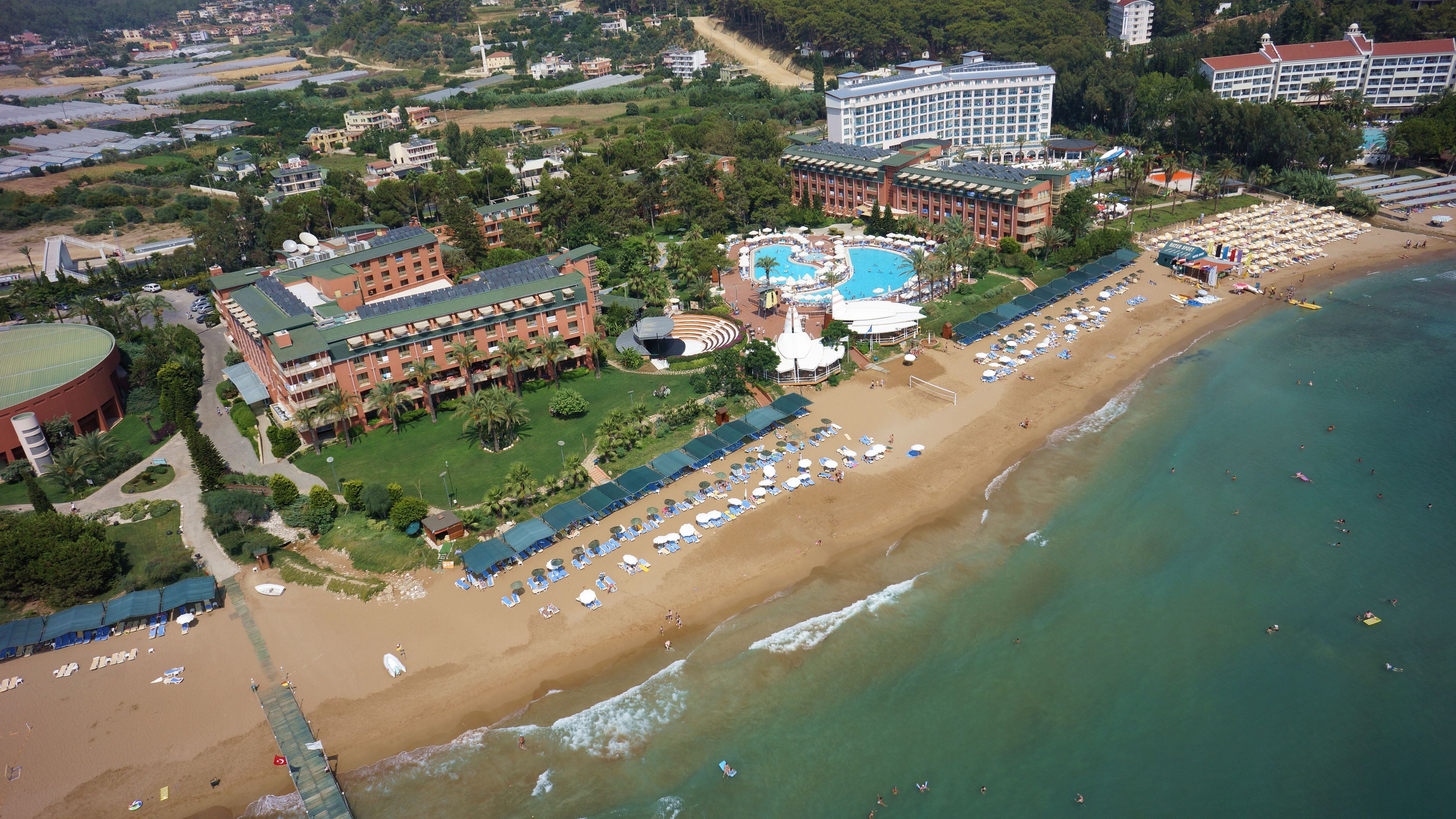 An aerial view of a resort with a large sandy beach, a swimming pool, and multiple hotel buildings.