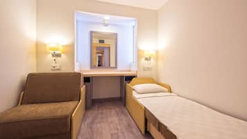 A small hotel room with a bed, a chair, a desk, and two wall-mounted lamps.