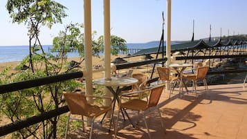 Eine Terrassenförmige Sitzgruppe am Strand mit Tischen und Stühlen, mit Blick auf das Meer und einen Steg.