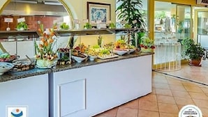 Zona de recepción de un hotel con mostrador de buffet, una planta grande en maceta y un cuadro en la pared.