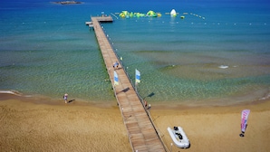 Un muelle de madera que se adentra en un mar azul cristalino, con una playa de arena al final.