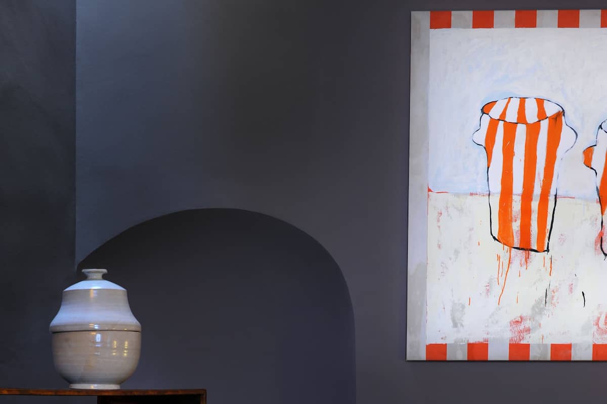 Una habitación con una cama, almohadas, un florero y un cuadro en la pared.