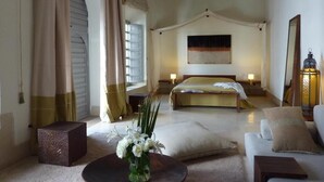 Un dormitorio espacioso con una cama grande, una zona de estar con sofá y una mesa de centro, y un jarrón decorativo con flores.