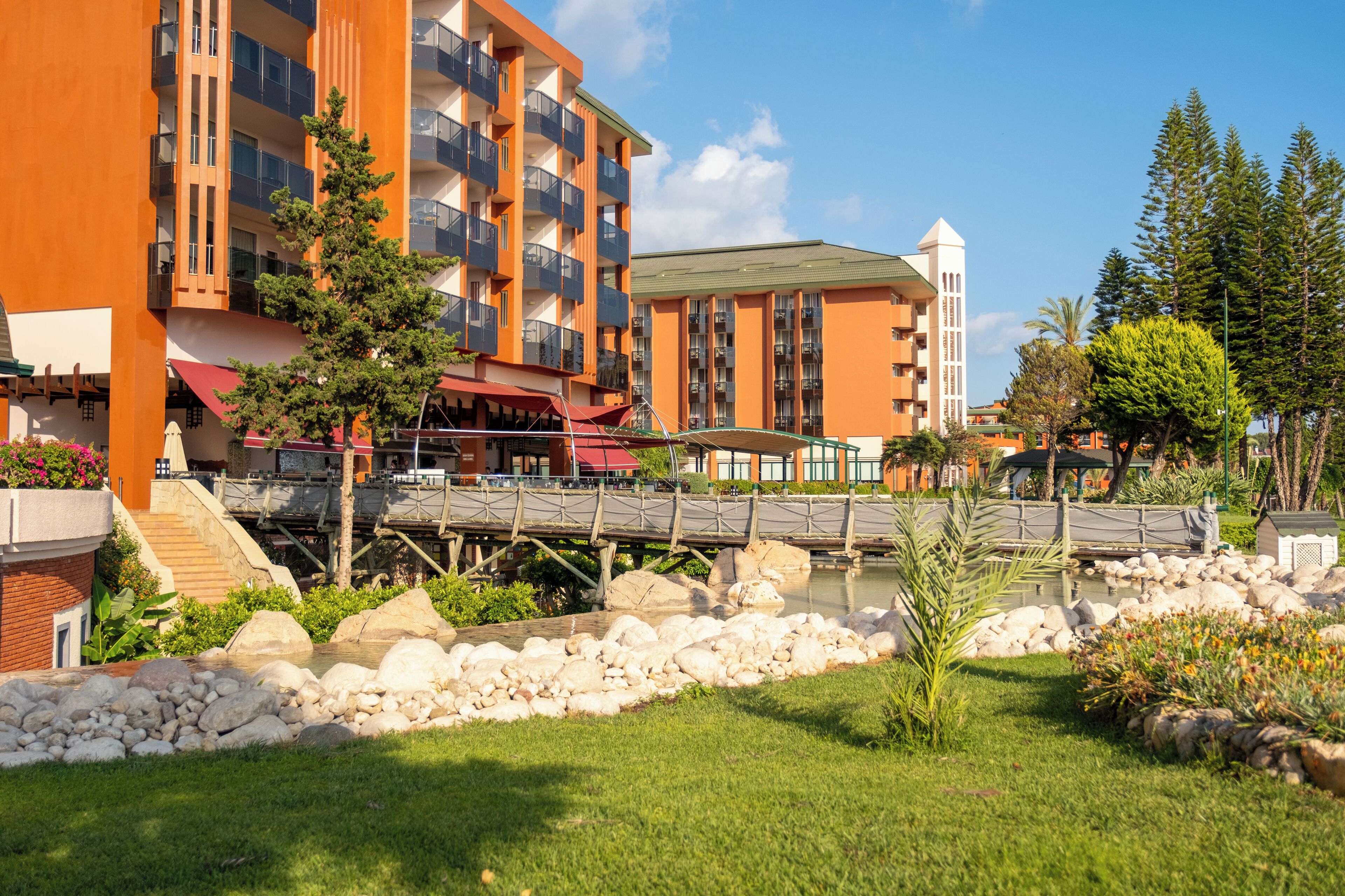 A multi-story hotel with balconies, a bridge over a water feature, and a landscaped garden.
