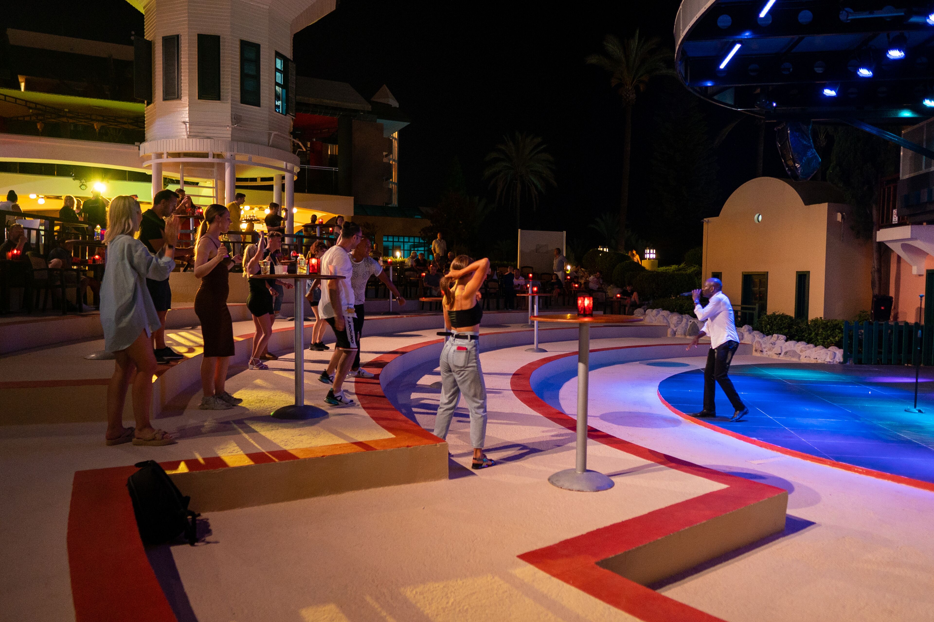 A nighttime outdoor area with a pool, seating, and a stage for performances.