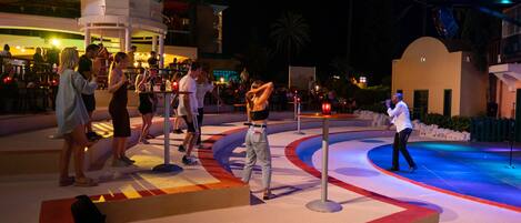 A nighttime outdoor area with a pool, seating, and a stage for performances.