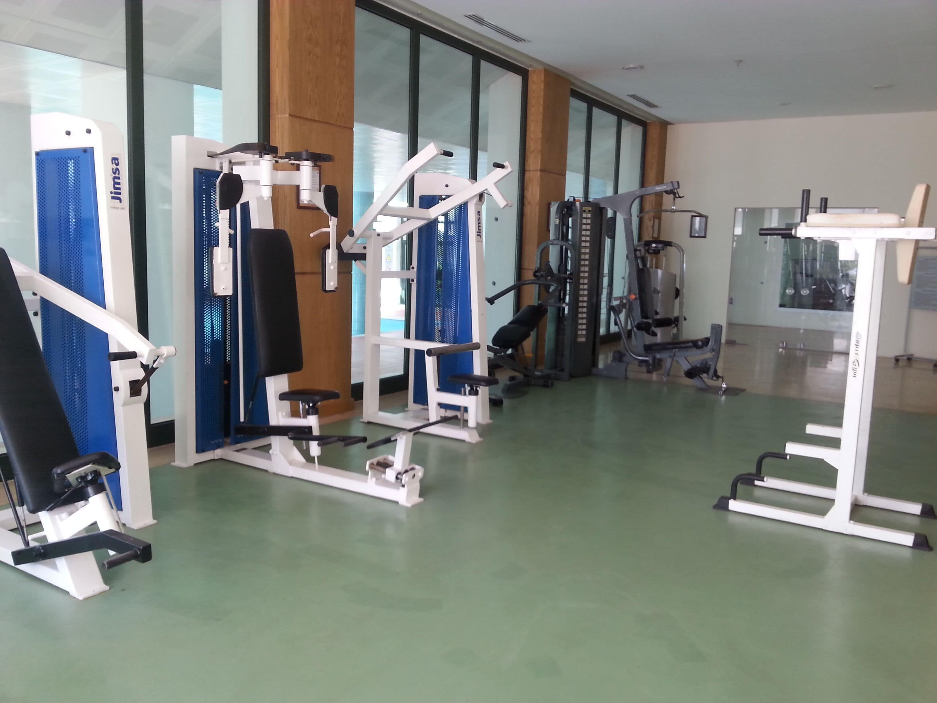 A gym with various exercise machines, including a bench press, a squat rack, and a cable machine.