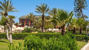 A landscaped garden with palm trees, a building with a red facade, and outdoor seating areas.