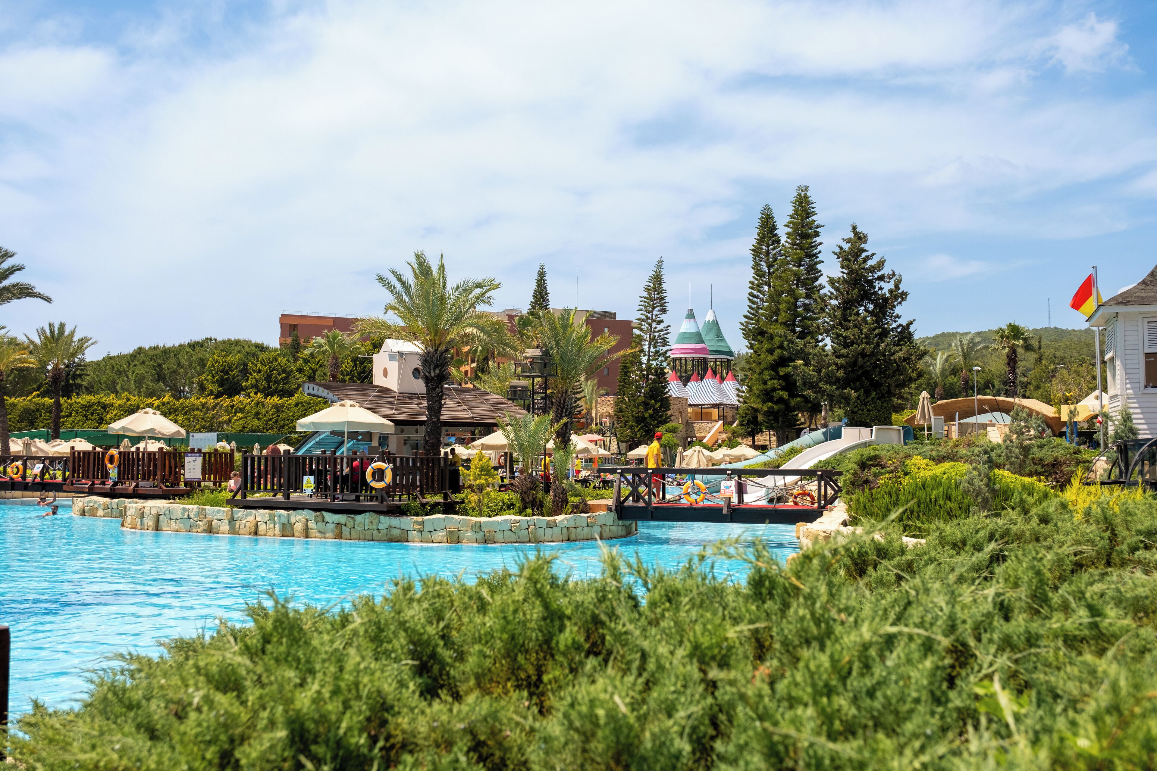 A swimming pool with lounge chairs and umbrellas, surrounded by greenery and buildings.