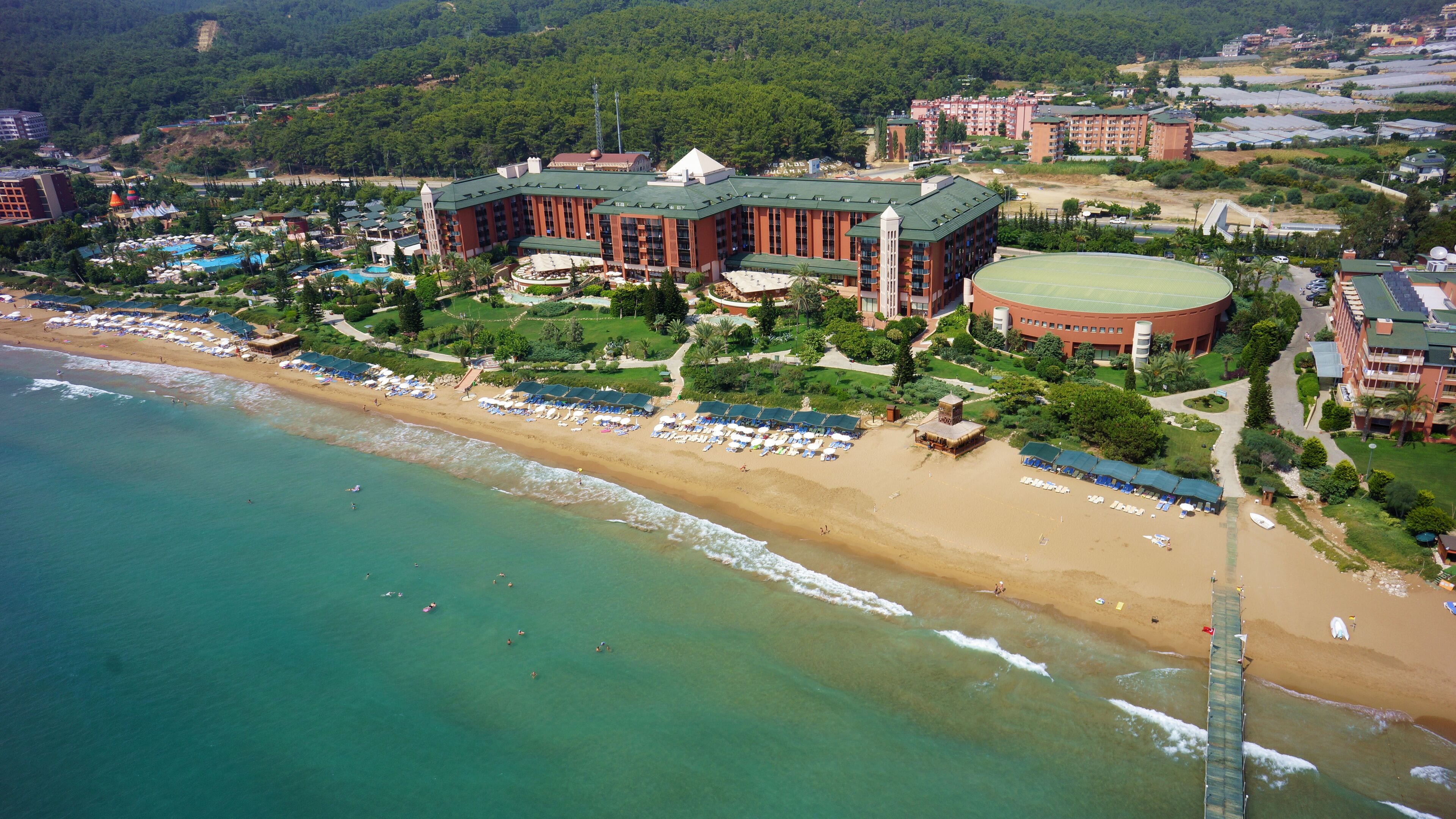 An aerial view of a coastal resort with a beach, a pool, and a large building with multiple floors.