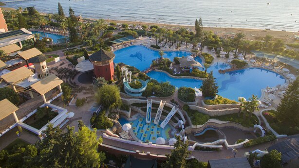 A resort with multiple swimming pools, a water slide, and a beach area.