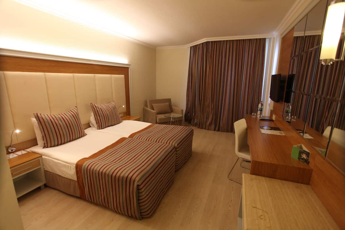 A hotel room with a large bed, a desk, a chair, and a television.