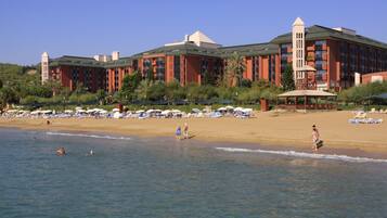 A hotel with multiple buildings, a beach with umbrellas, and people near the water.