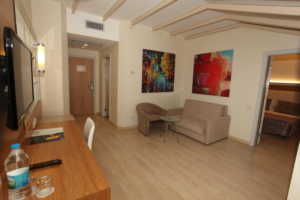 A hotel room with a wooden dining table, a sofa, a small round table, and two paintings on the wall.