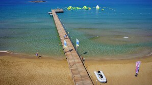 A wooden pier extending into a clear blue sea with a sandy beach at the end.