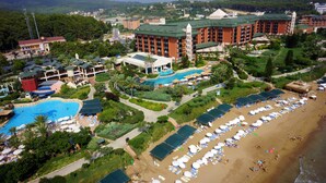 A resort with a large swimming pool, multiple beach areas with sun loungers, and a central building with a green roof.