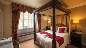 Un lit à baldaquin avec une couvre-lit rouge, une table de chevet avec une lampe et une fenêtre avec des rideaux.