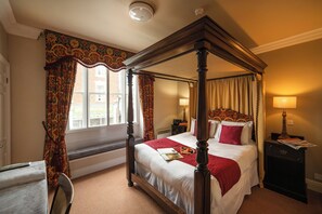 Un lit à baldaquin avec une couvre-lit rouge, une table de chevet avec une lampe et une fenêtre avec des rideaux.