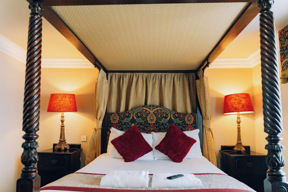 Un lit à baldaquin, deux lampes rouges et une tête de lit à motifs.