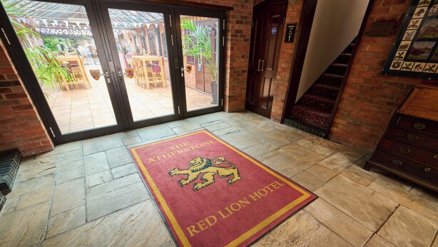 L’entrée d’un hôtel, avec un tapis rouge orné d’un lion, un mur de briques et un escalier.