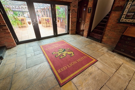 A hotel entrance with a red lion carpet, a brick wall, and a staircase.. The Atherstone Red Lion Hotel