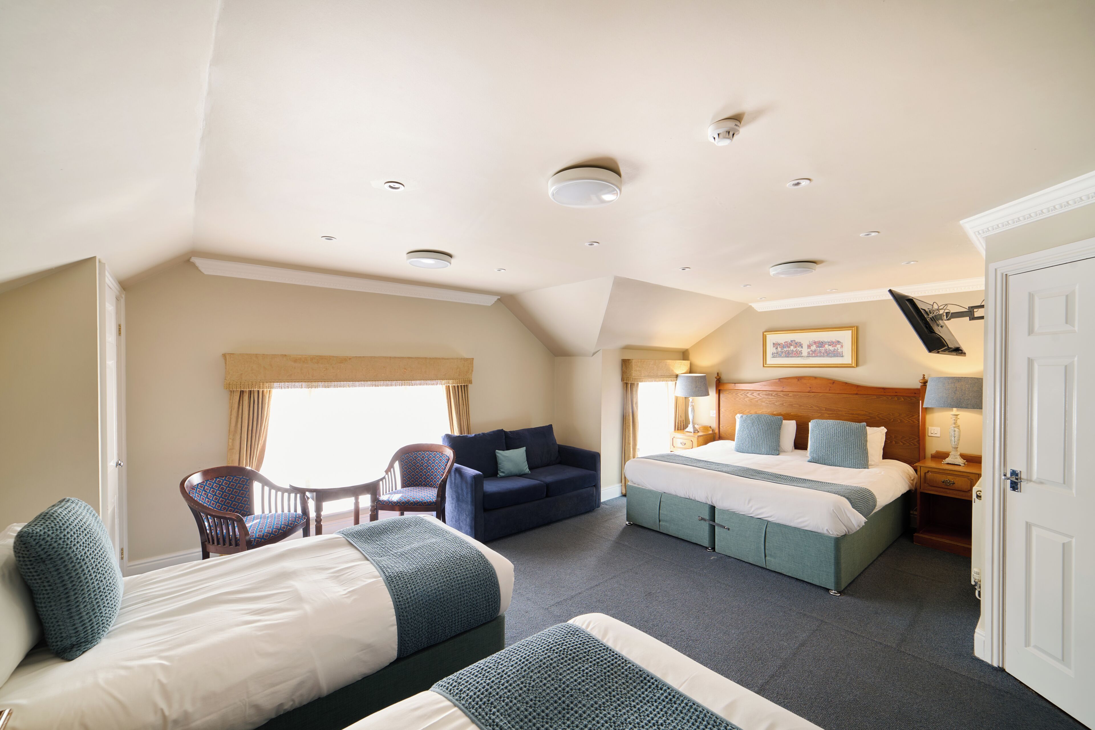 A hotel room with a bed, two sofas, a chair, a bedside table with lamps, and a window with curtains.