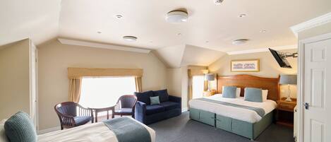 A hotel room with a bed, two sofas, a chair, a bedside table with lamps, and a window with curtains.