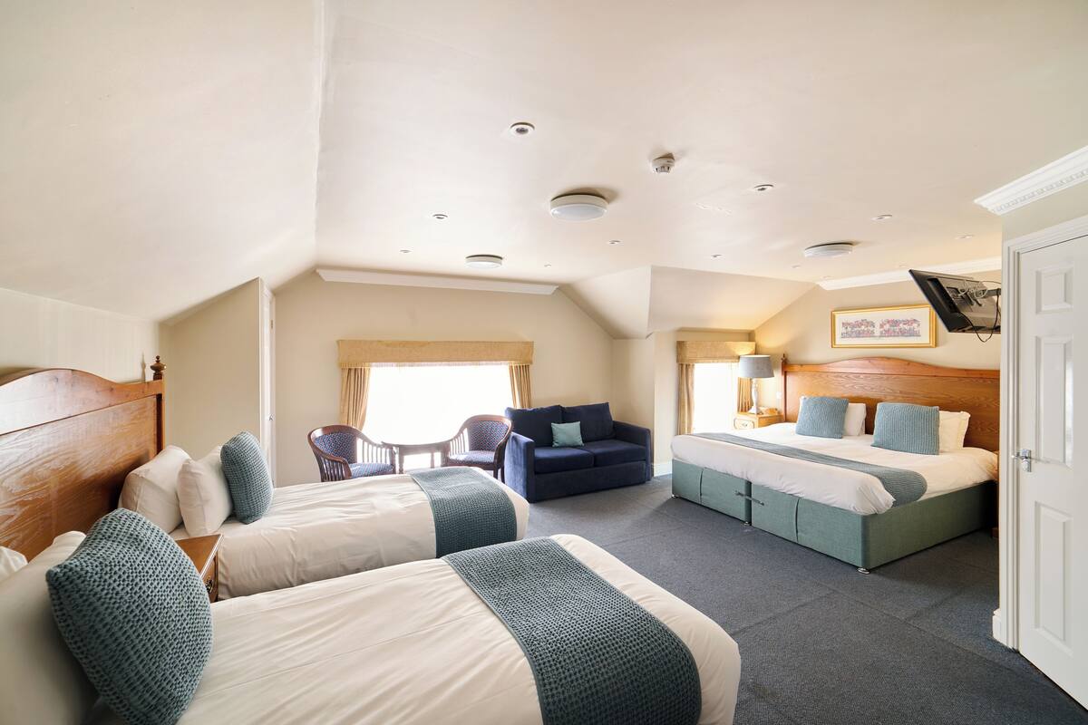 Une chambre d’hôtel avec deux lits, un canapé, une table à manger et un téléviseur fixé au mur.