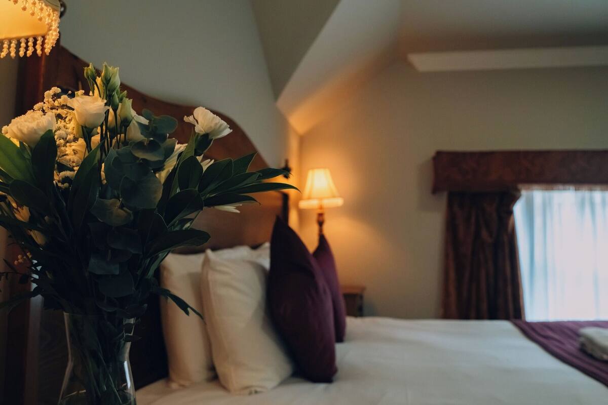 Une chambre d’hôtel avec un lit, une table de chevet avec une lampe et un vase de fleurs.