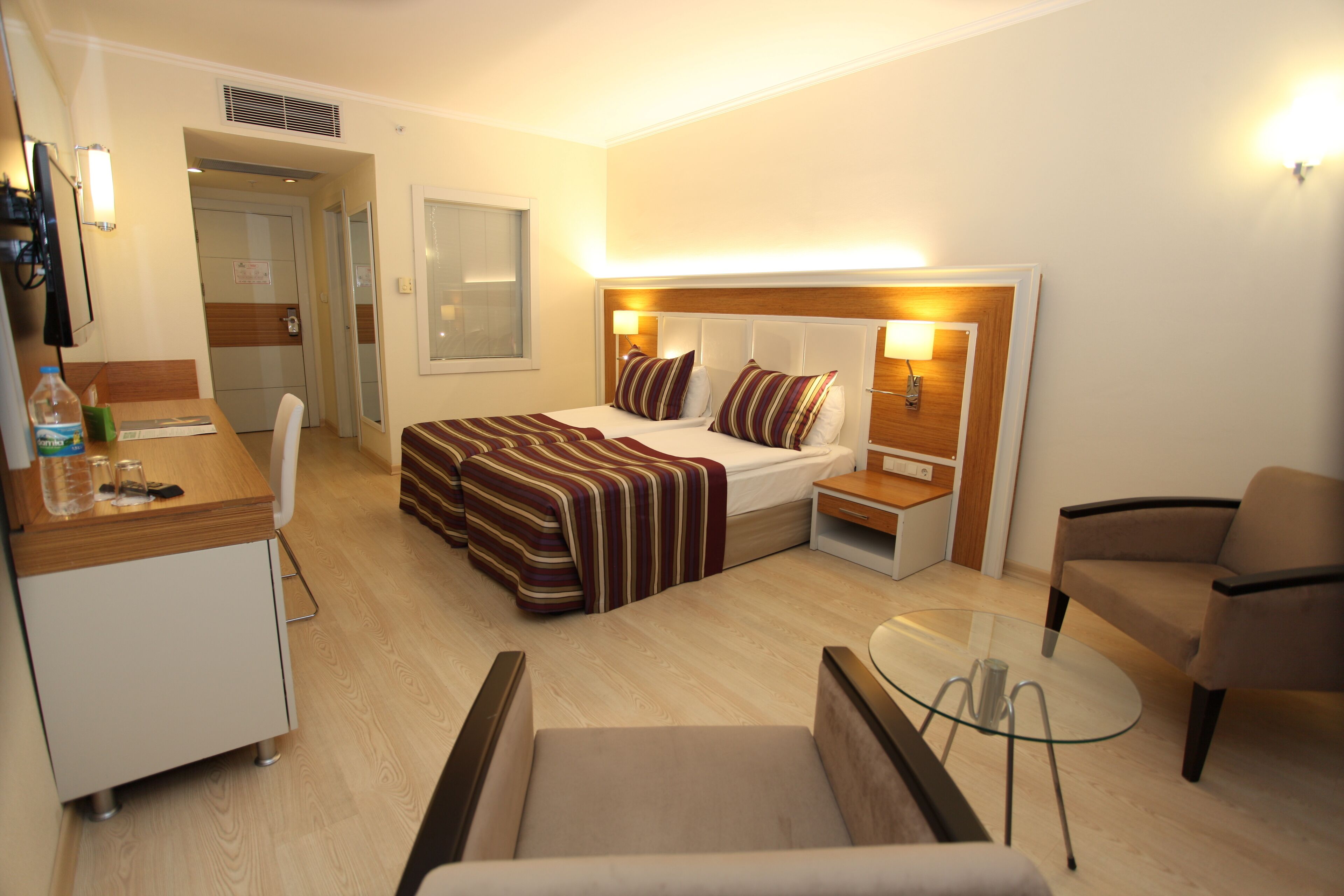 A hotel room with a bed, bedside tables, a chair, a small table, and a desk with a chair.