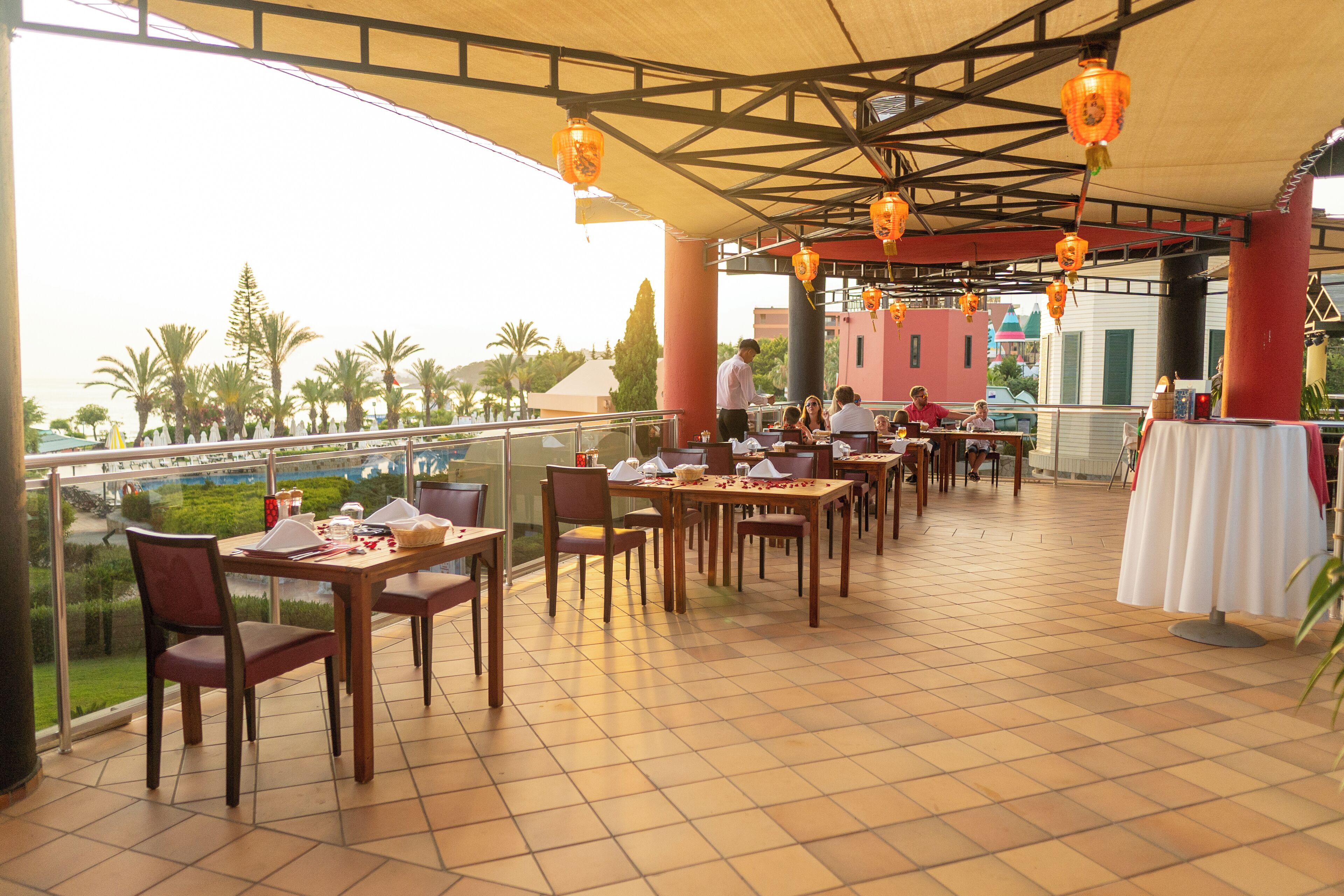 An outdoor dining area with tables and chairs, a view of the landscape, and hanging lanterns.