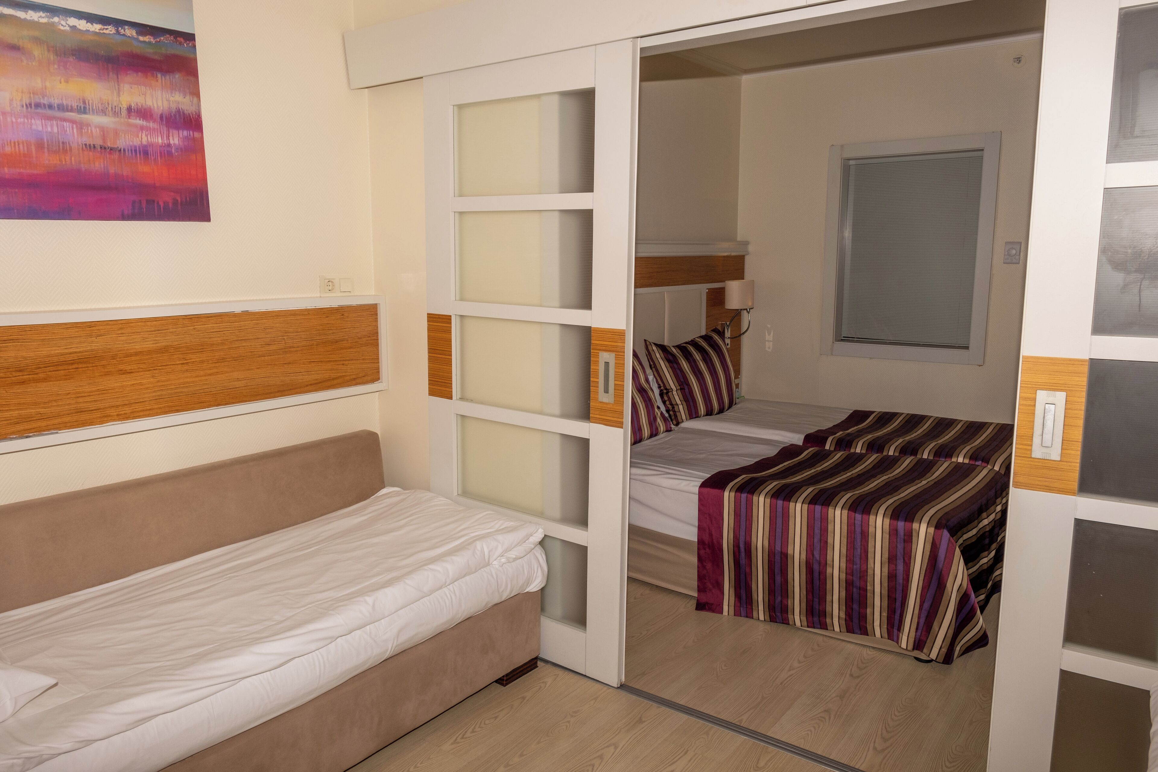 A compact room with a single bed, a small sofa, and a window with blinds.