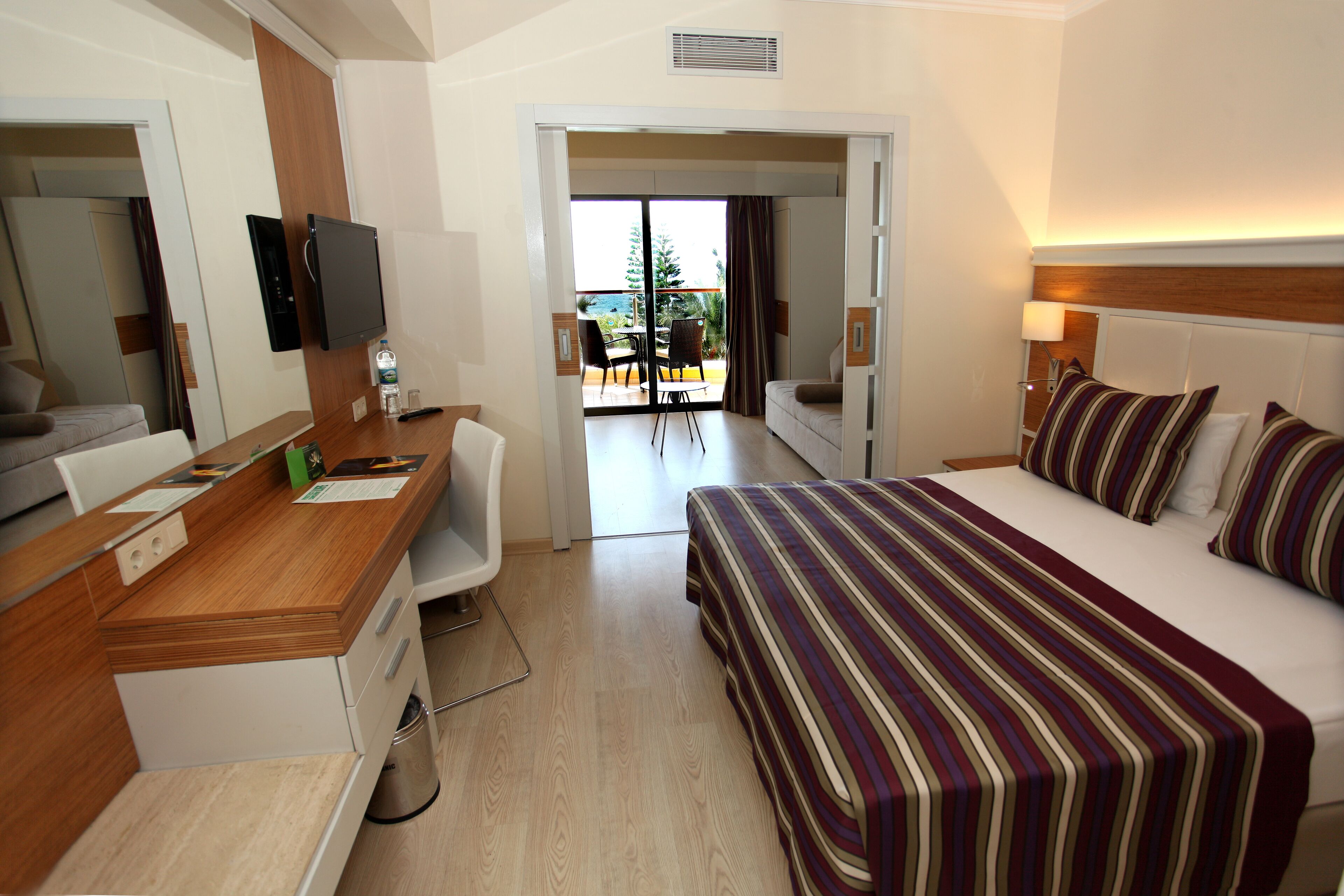A hotel room with a bed, a desk, a chair, a TV, and a view of the outdoors.