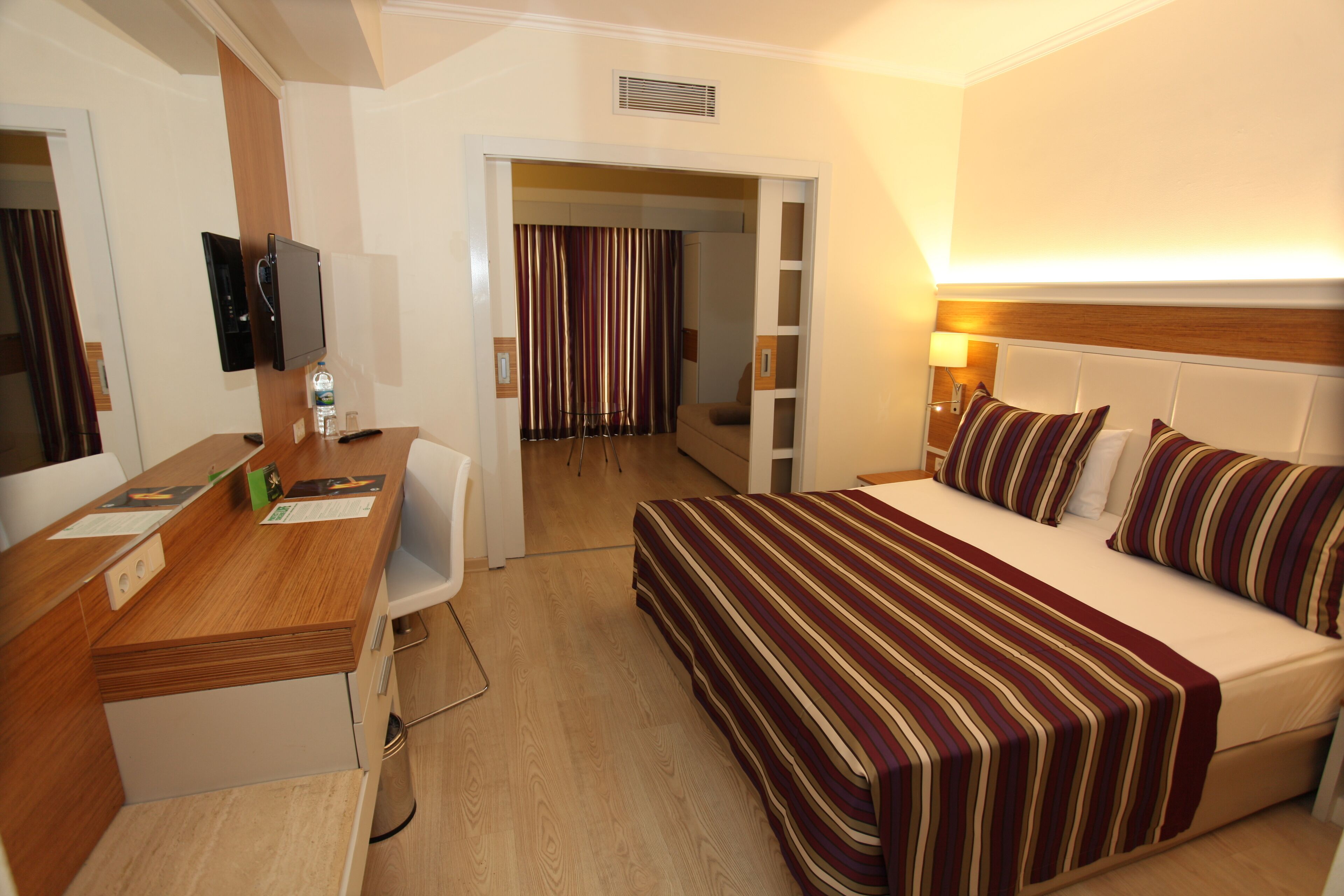 Habitación de hotel con cama, escritorio, silla, televisión y baño visible a través de una puerta abierta.