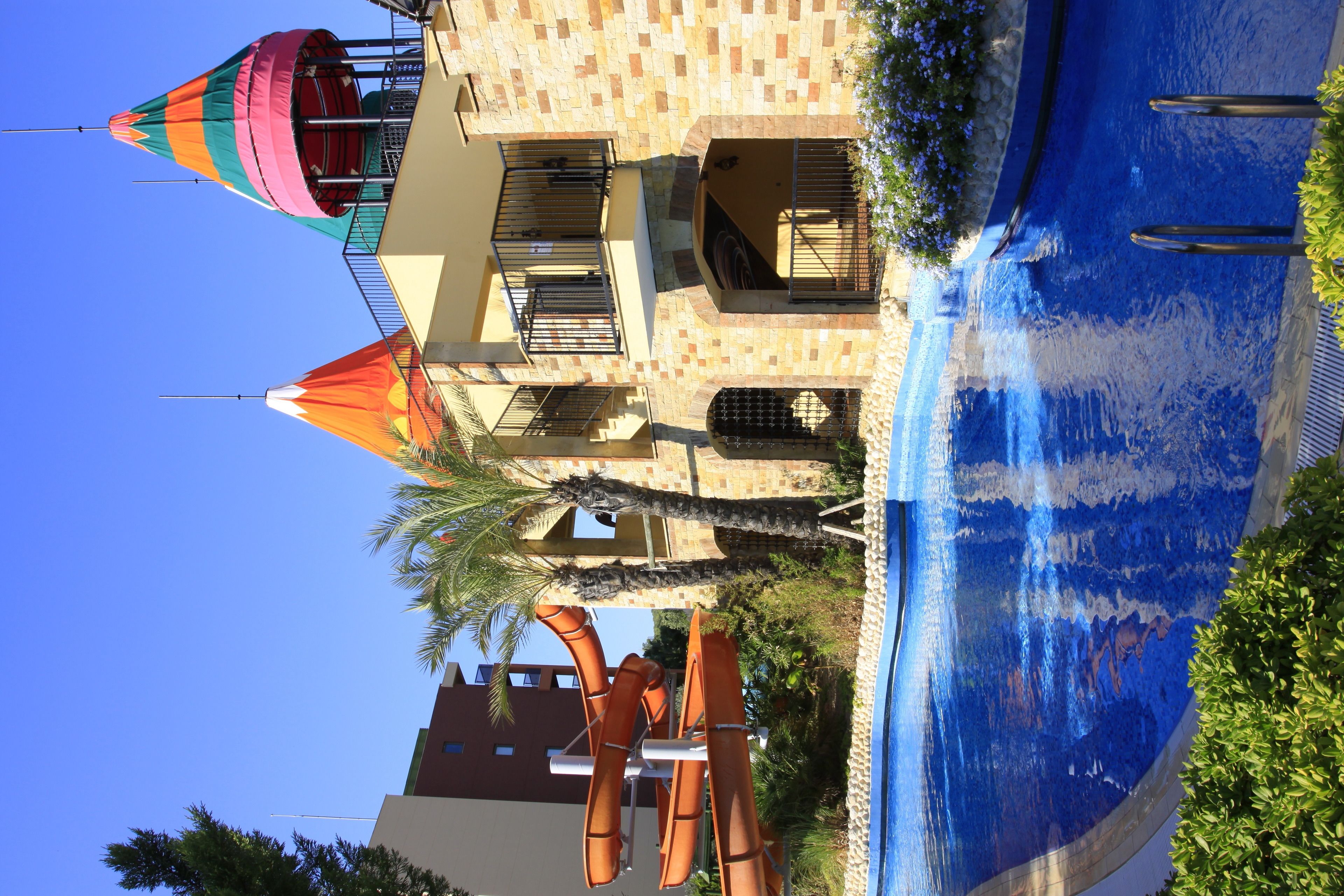 Un área de piscina con tobogán de agua, palmeras y un edificio con balcones.