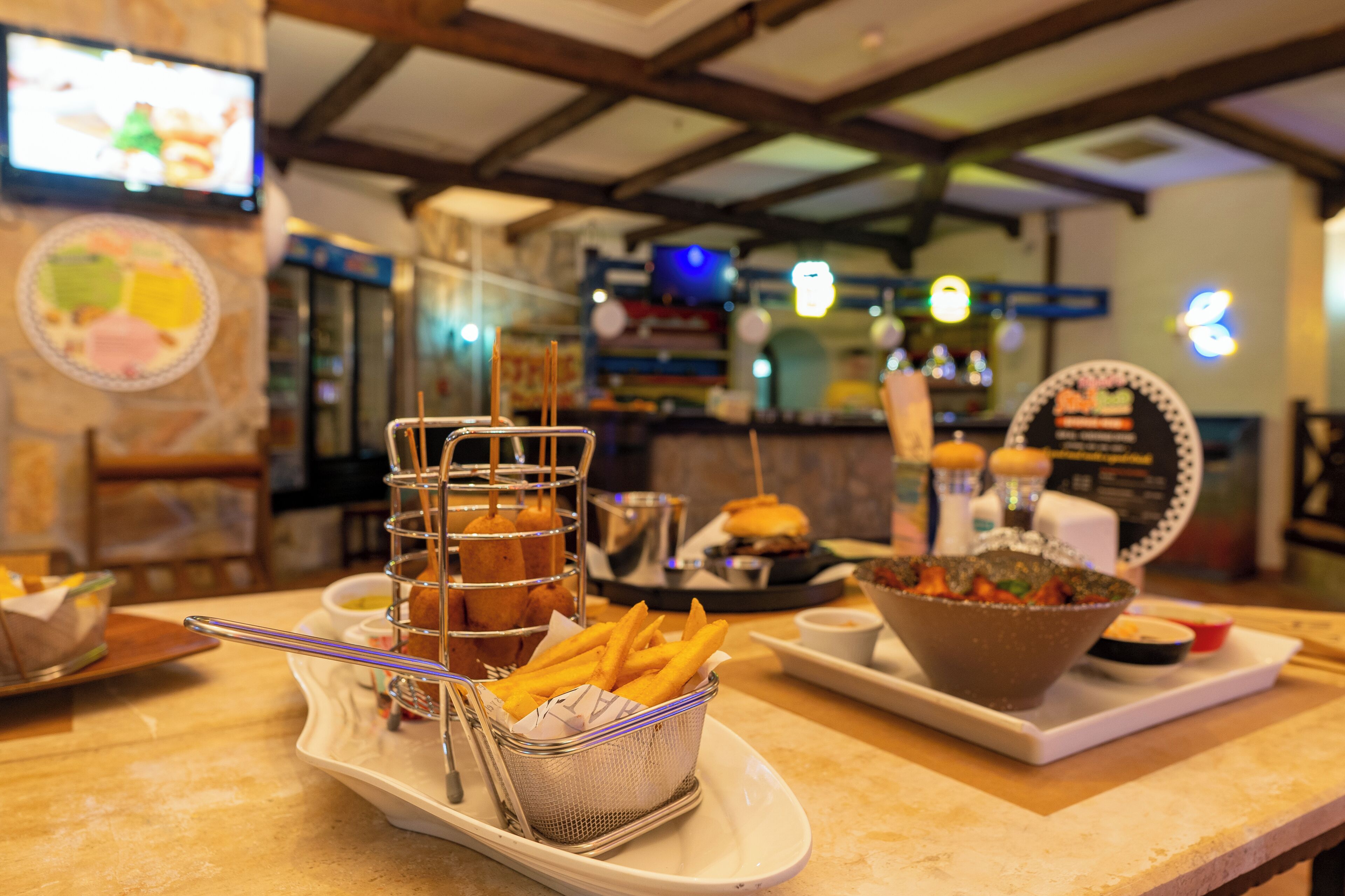 A restaurant counter with a tray of food including fries, a basket of corn dogs, and a bowl of salad.